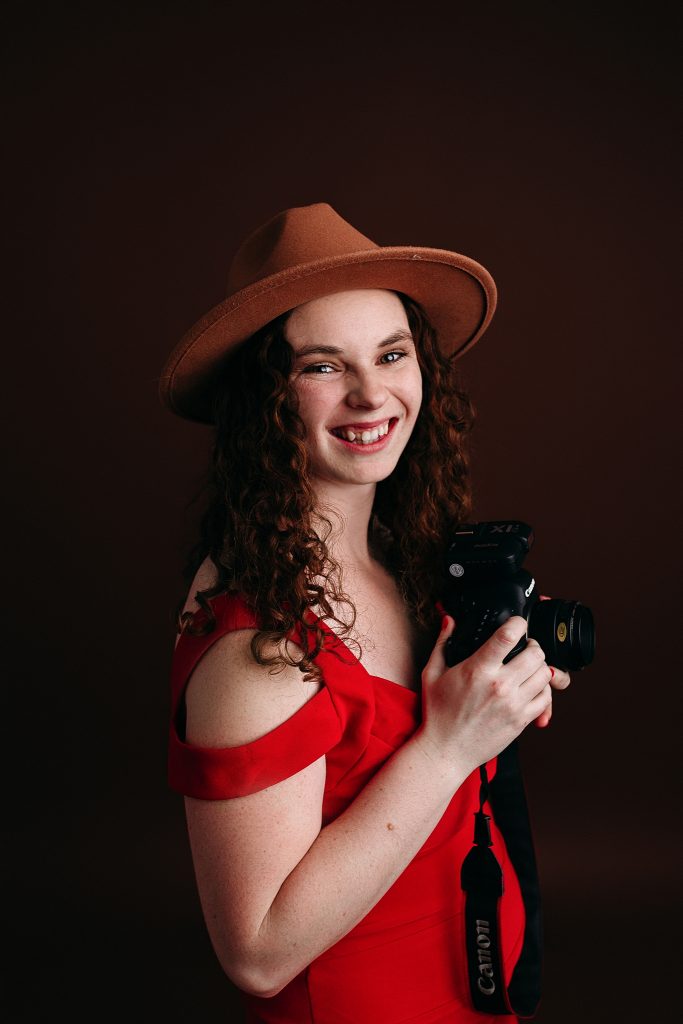 newborn photographer in red dress holding camera