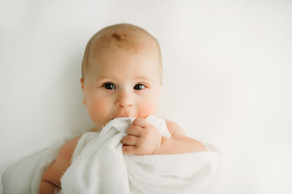 six month old baby chewing on blanket for baby photos