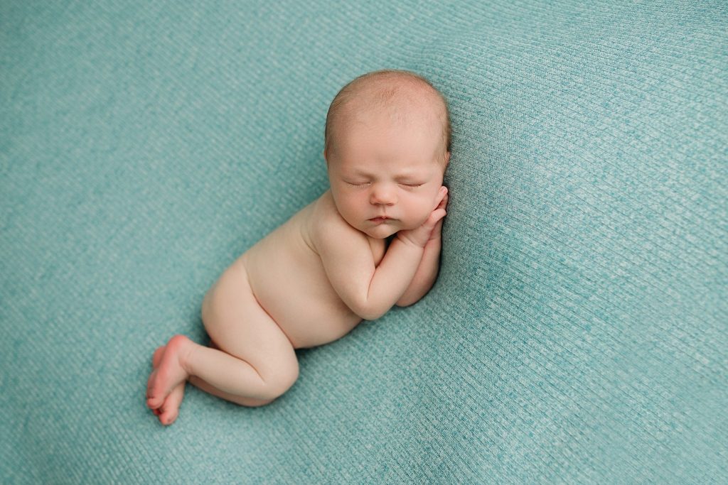 newborn boy sleeping with hands by cheek