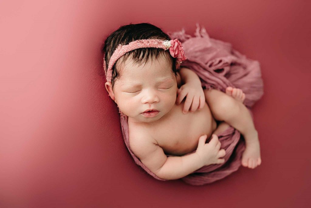 baby in bow sleeping on pink