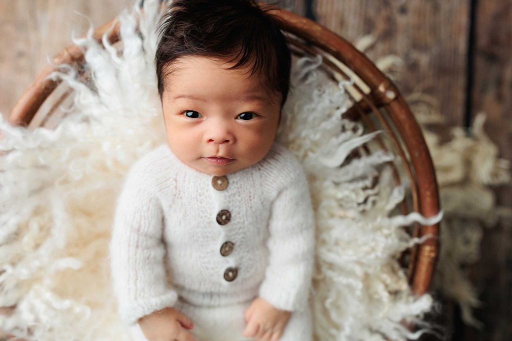 wide eyed baby in pjs on fur in wooden bowl