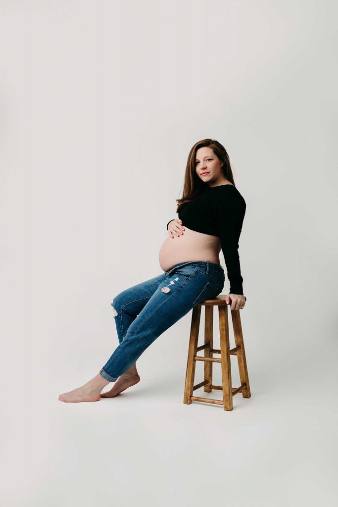 classy chic maternity photo on stool wearing jeans and a crop top