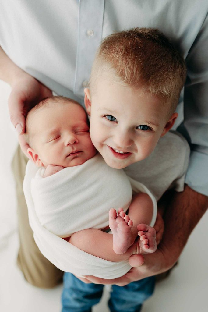 big brother smiles holding baby