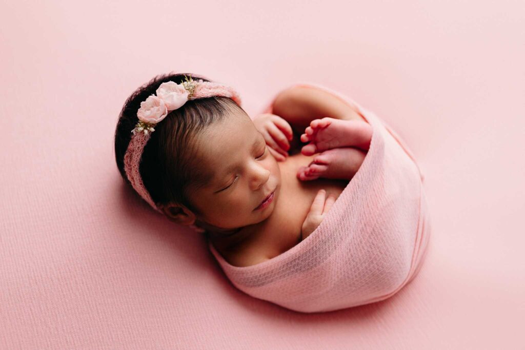 newborn swaddled in pink on fabric
