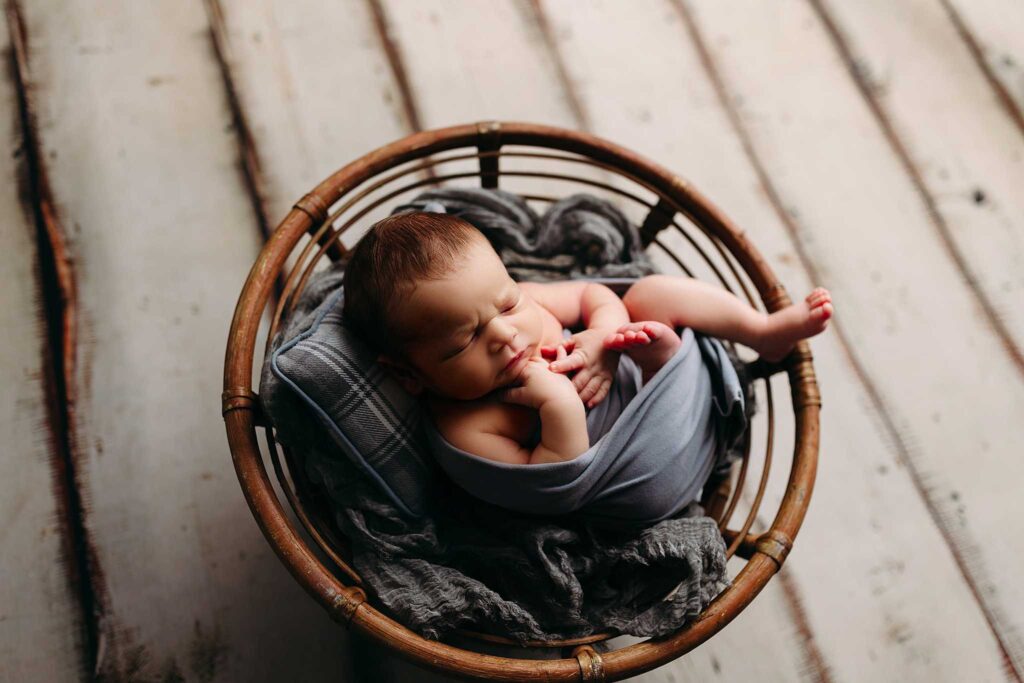 newborn boy swaddled in gray on papasan chair with cream floor