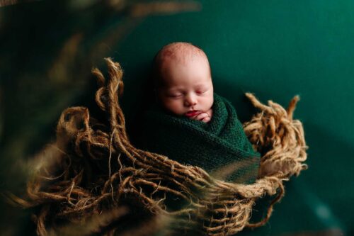 newborn in swaddled in green knit wrapped in burlap