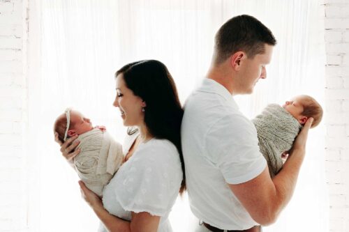 twin newborns swaddled in parents arms