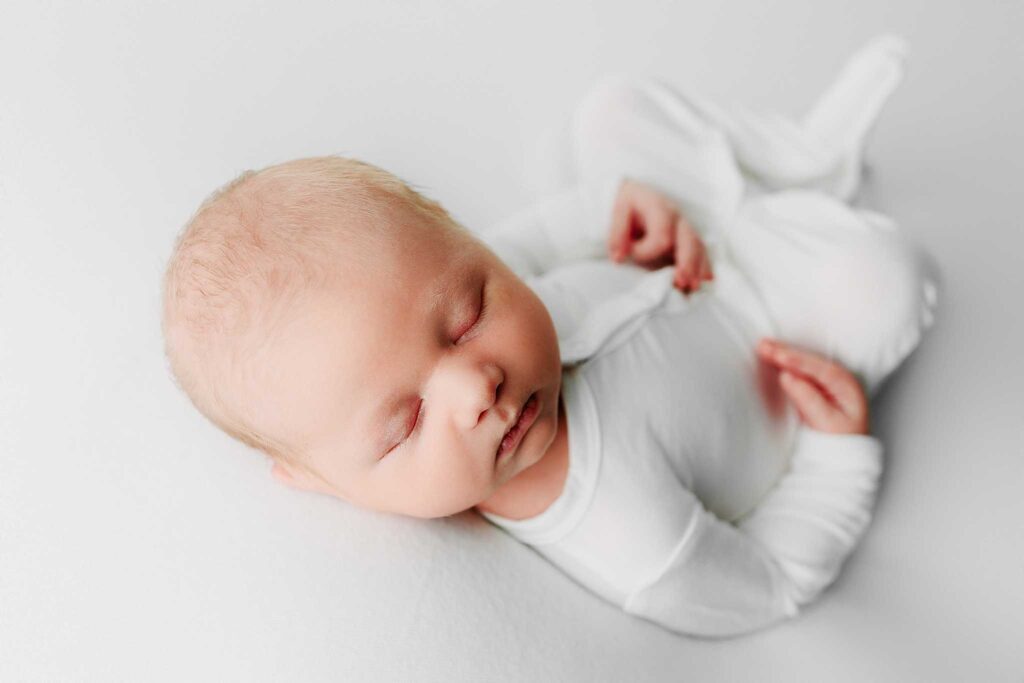 newborn in white button pjs sleeping on white