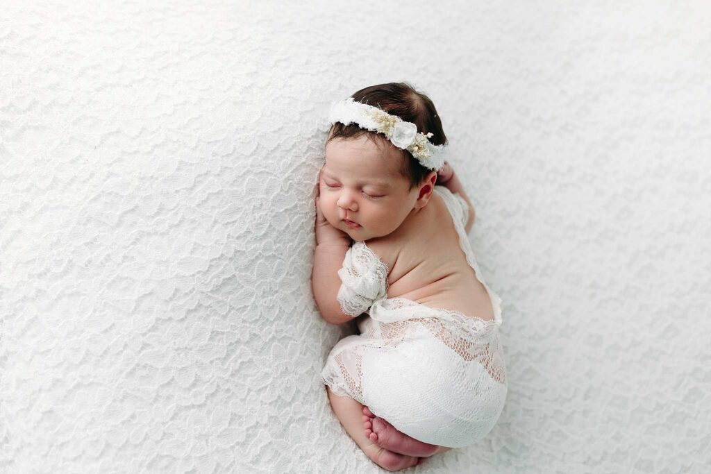 newborn in lace sleeping on white backdrop