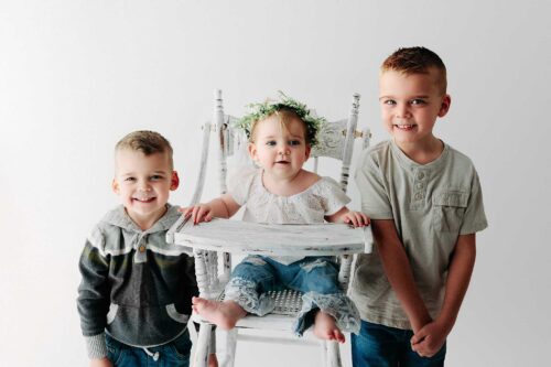 siblings standing near high chair by window white backdrop