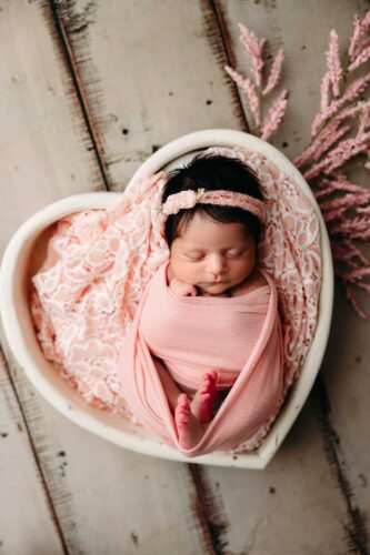 newborn girl swaddled in pink in pink heart bowl