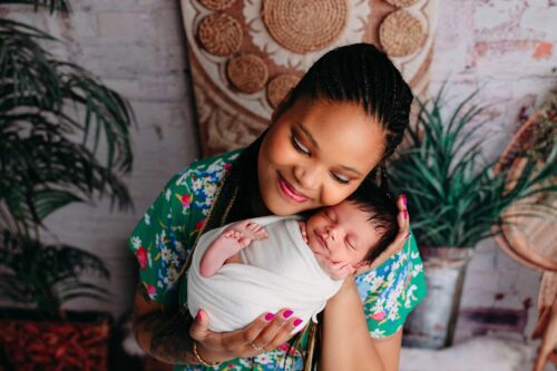 dark skinned mom snuggling wrapped baby boho green backdrop