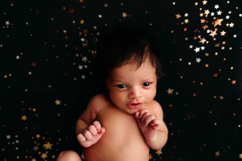 wide eyed baby boy on black blanket with gold stars