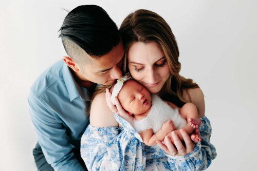 family snuggling newborn girl in white romper