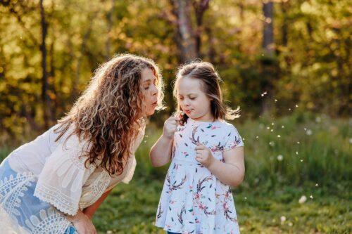 mom and daughter outside blowing dandilions