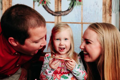 girl holding christmas cookie out to parents