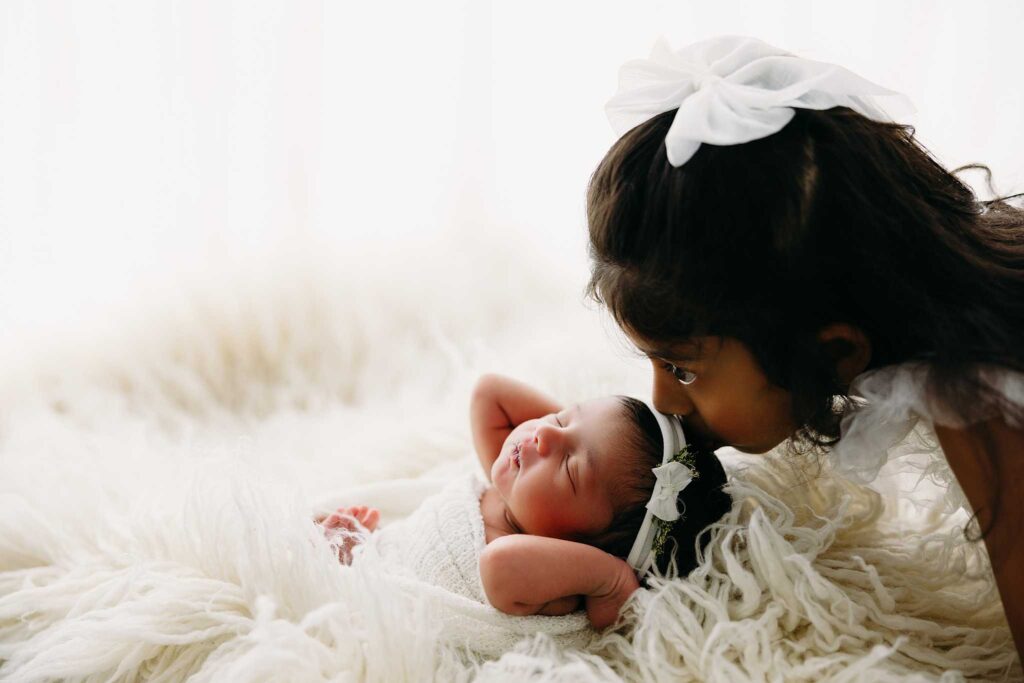 sister kisses newborn flokati